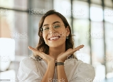 Cheerful business woman with glasses posing with her hands under her face showing her smile in an office. Playful hispanic female entrepreneur looking happy and excited at workplace Happiness Stock Photo